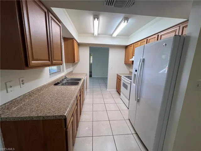 Kitchen with stainless steel fridge with ice dispenser, sink, light tile patterned flooring, ornamental molding, and white range with electric stovetop