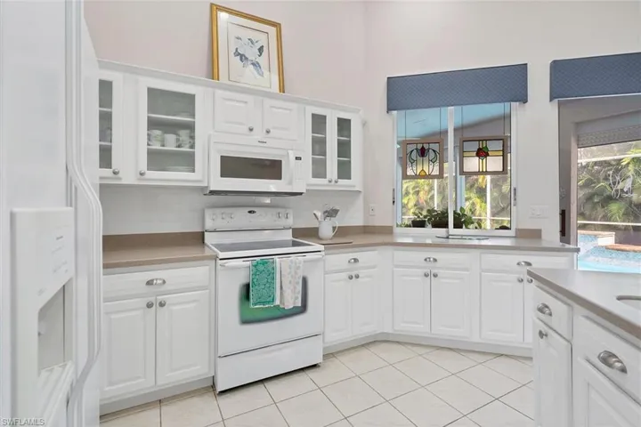 Kitchen with white appliances, backsplash, light tile patterned floors, and white cabinets