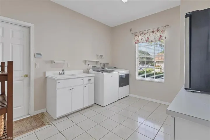 Clothes washing area with light tile patterned floors, cabinets, washer and clothes dryer, and sink