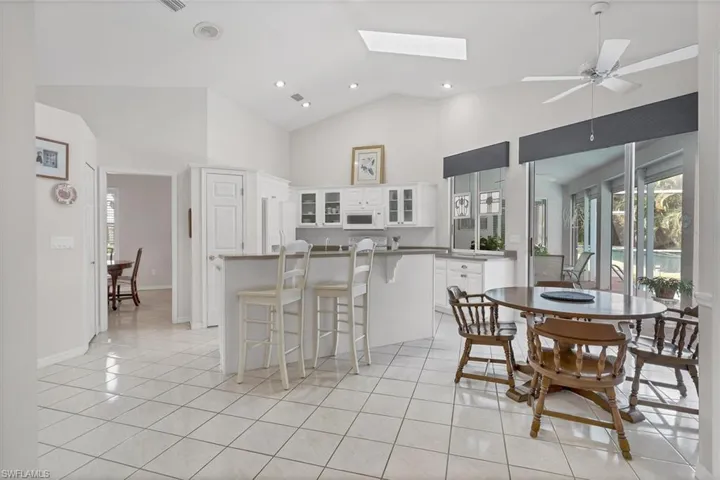 Tiled dining space with ceiling fan, high vaulted ceiling, and a skylight
