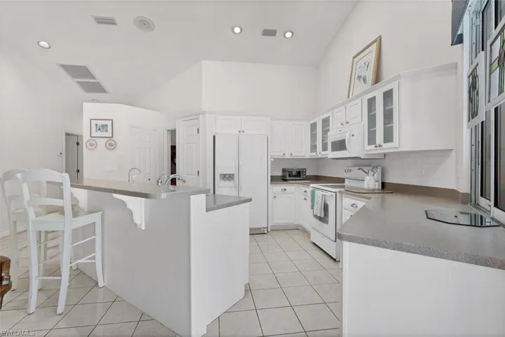 Kitchen with white cabinetry, white appliances, a kitchen bar, an island with sink, and light tile patterned flooring