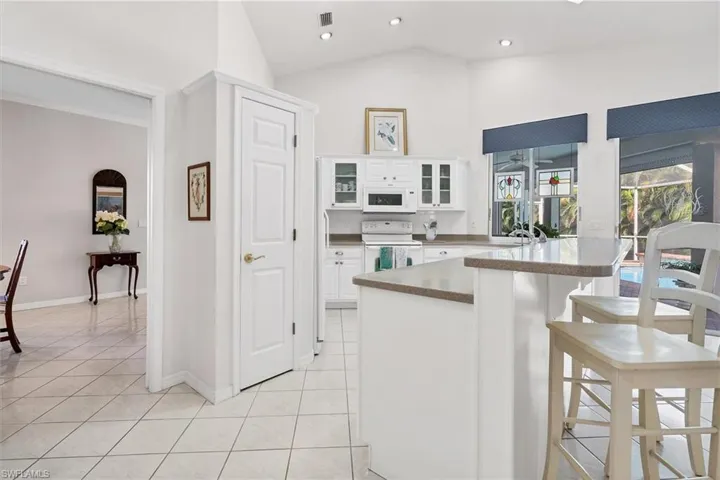 Kitchen featuring a breakfast bar area, white appliances, light tile patterned floors, lofted ceiling, and white cabinets