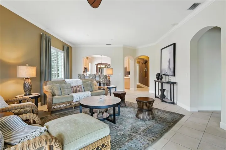Living area featuring crown molding, arched walkways, light tile patterned flooring, and a chandelier