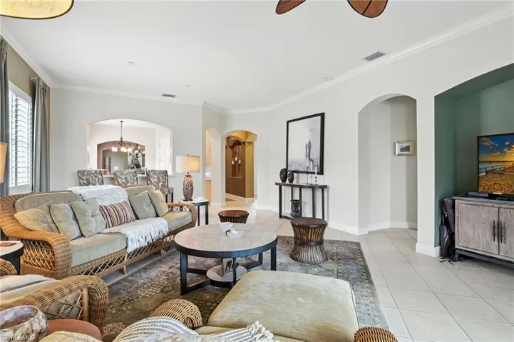 Tiled living area featuring ornamental molding, arched walkways, a chandelier, and ceiling fan