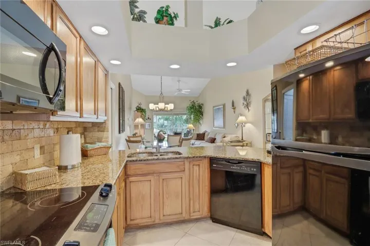 Kitchen with decorative backsplash, black appliances, open floor plan, recessed lighting, and light stone countertops