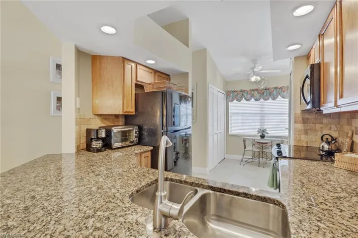 Kitchen featuring decorative backsplash, light stone countertops, black appliances, ceiling fan, and recessed lighting