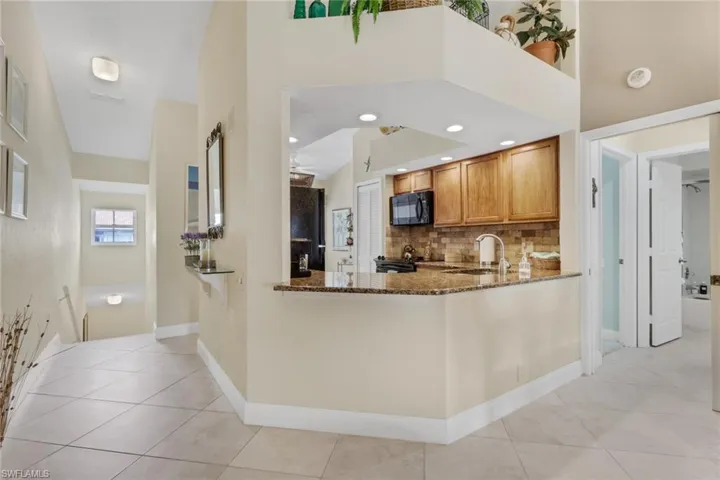 Kitchen featuring brown cabinets, dark stone countertops, black appliances, a peninsula, and backsplash