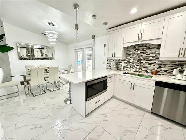 Kitchen with white cabinets, stainless steel appliances, a peninsula, ornamental molding, and light marble finish floors