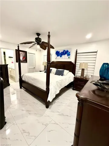 Bedroom with ensuite bath, a ceiling fan, and light marble finish flooring