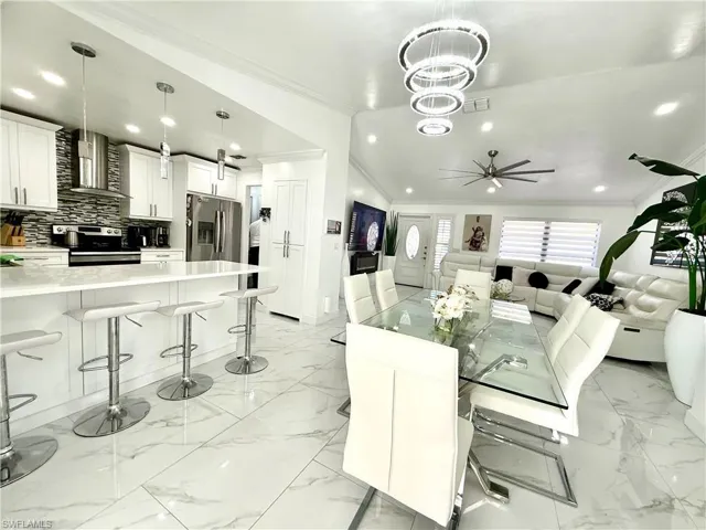 Dining room featuring crown molding, light marble finish flooring, hanging lights, a ceiling fan, and lofted ceiling