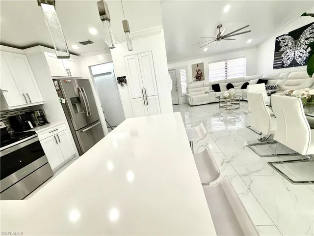 Kitchen featuring ornamental molding, white cabinets, stainless steel appliances, pendant lighting, and light marble finish flooring