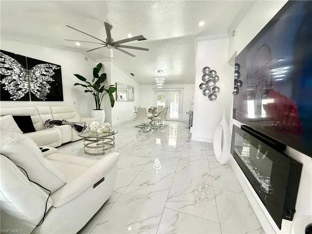 Living room with a ceiling fan, light marble finish flooring, ornamental molding, vaulted ceiling, and recessed lighting