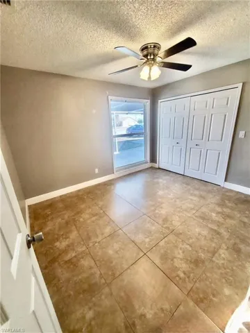 Unfurnished bedroom with a textured ceiling, ceiling fan, a closet, and tile patterned floors