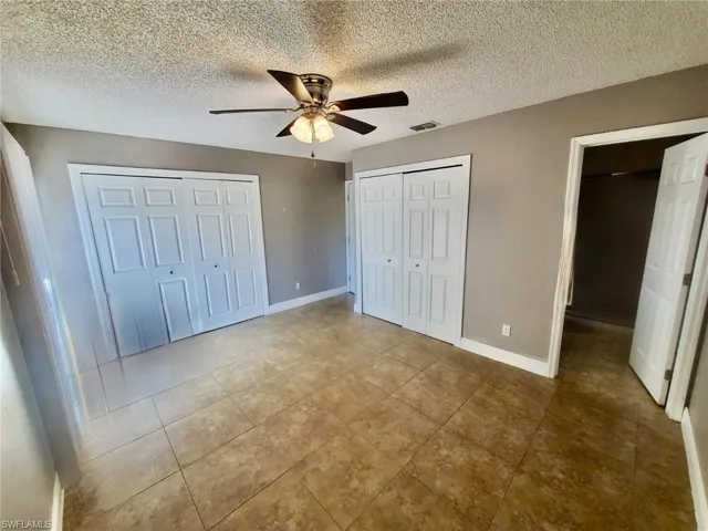 Unfurnished bedroom with a ceiling fan, a textured ceiling, two closets, and light tile patterned floors