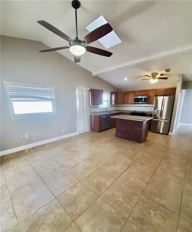 Kitchen featuring stainless steel appliances, light countertops, a center island, a ceiling fan, and open floor plan