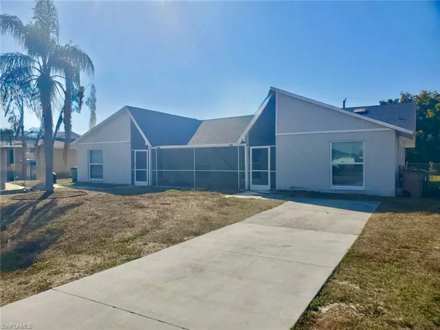View of front facade featuring stucco siding, roof with shingles, a front lawn, and concrete driveway