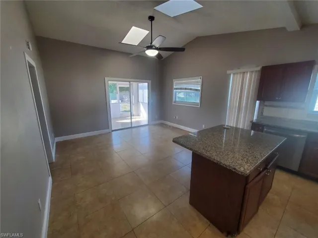 Kitchen featuring a skylight, a center island, dark stone counters, a ceiling fan, and stainless steel dishwasher