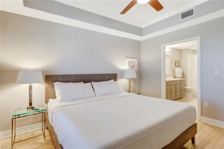 Bedroom with light wood-style floors, ensuite bath, a ceiling fan, a tray ceiling, and ornamental molding