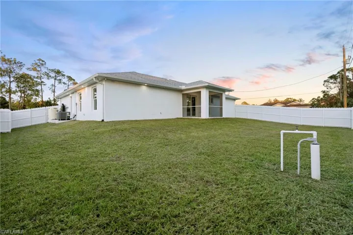 Back house at dusk with a lawn and central AC unit