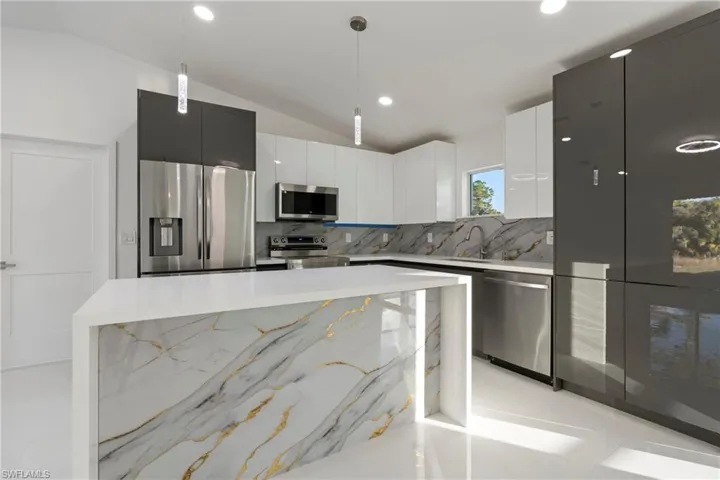 Kitchen featuring light stone countertops, backsplash, pendant lighting, lofted ceiling, and appliances with stainless steel finishes