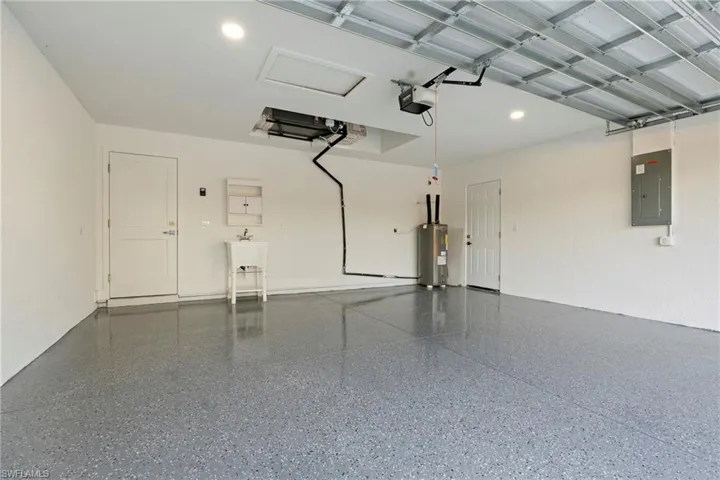 Garage featuring electric panel, electric water heater, and a garage door opener