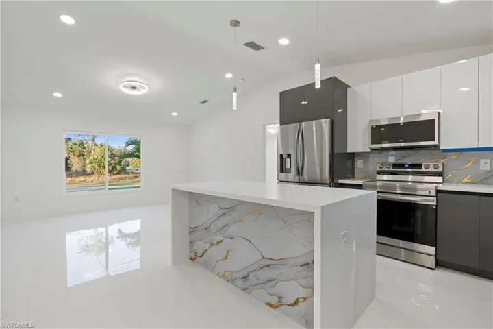 Kitchen featuring lofted ceiling, hanging light fixtures, decorative backsplash, white cabinetry, and stainless steel appliances