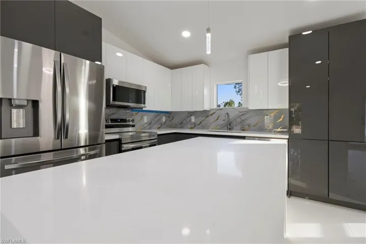 Kitchen featuring tasteful backsplash, white cabinetry, hanging light fixtures, and stainless steel appliances