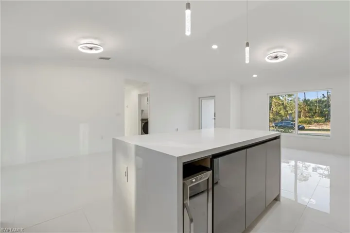 Kitchen featuring gray cabinetry, beverage cooler, light tile patterned floors, decorative light fixtures, and washer / dryer