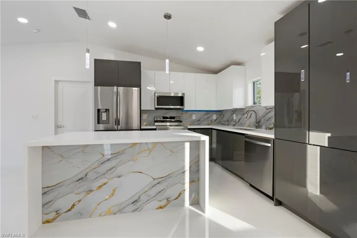 Kitchen featuring stainless steel appliances, backsplash, vaulted ceiling, decorative light fixtures, and white cabinets
