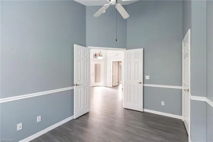 Empty room featuring ceiling fan, dark wood-type flooring, and a towering ceiling