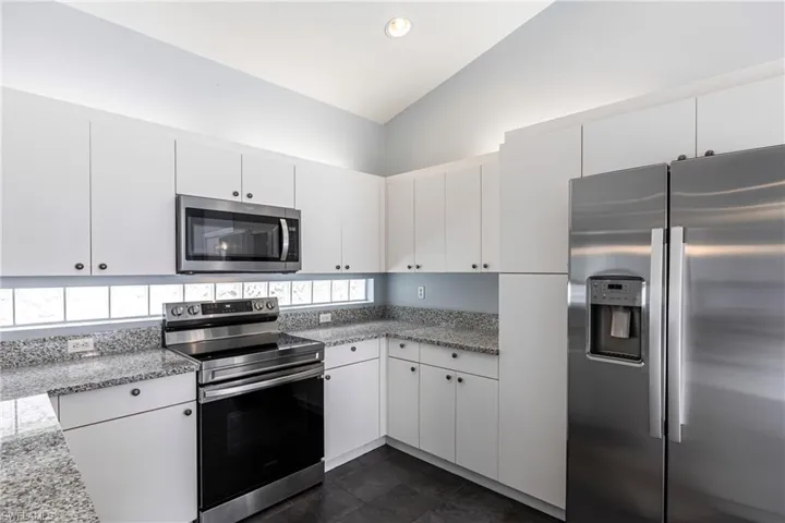 Kitchen with dark tile patterned flooring, stainless steel appliances, plenty of natural light, white cabinets, and vaulted ceiling