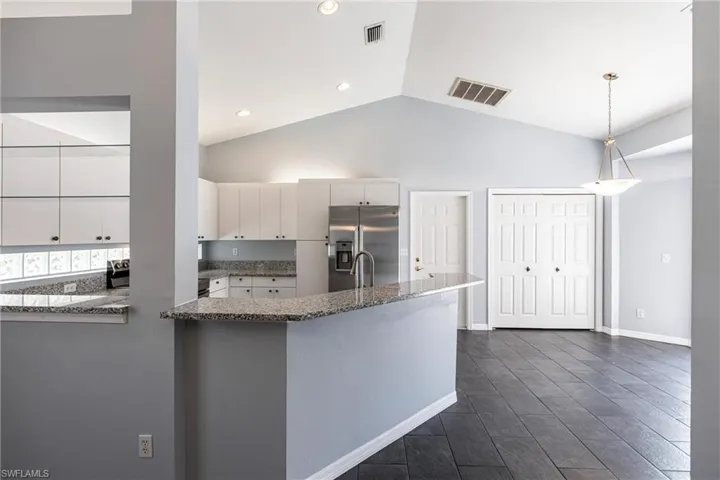 Kitchen with white cabinetry, pendant lighting, dark stone countertops, stainless steel fridge, and high vaulted ceiling