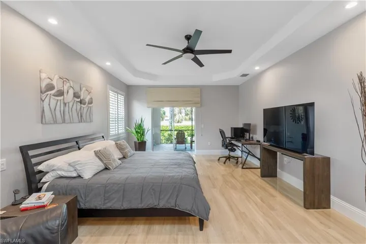 large owners suite with a raised tray ceiling, light ceramic tile flooring, ceiling fan, and access to lanai