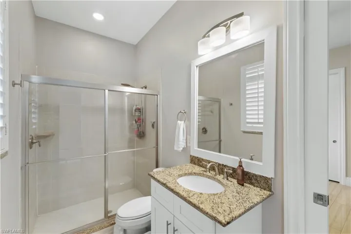 Bathroom featuring vanity with granite counter top, toilet, and walk in shower with granite accents