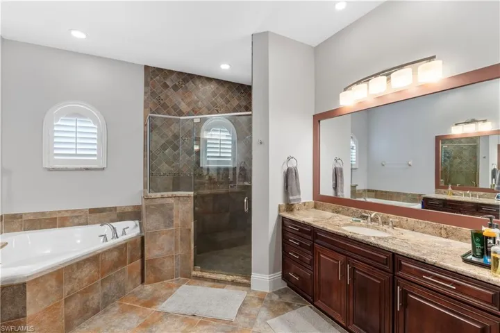 Bathroom with dual vanities, independent shower with floor to ceiling premium tile, soaking tub, recessed and modern light fixtures and light ceramic tile flooring