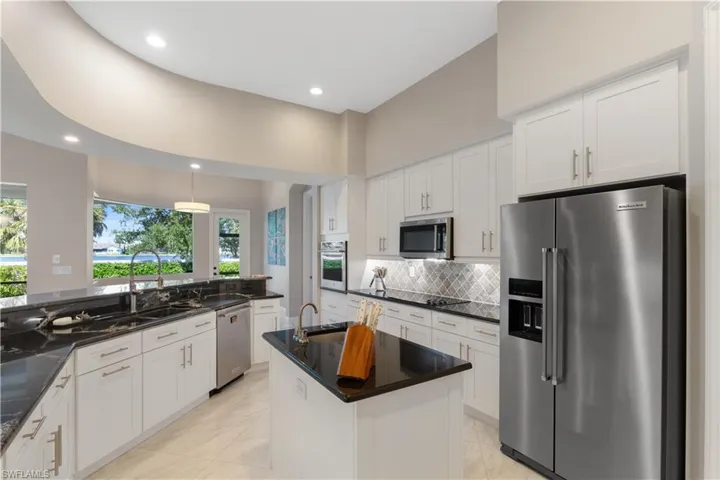 Kitchen with a kitchen island with sink, stainless steel appliances, sink, decorative backsplash, and black cloud granite countertops
