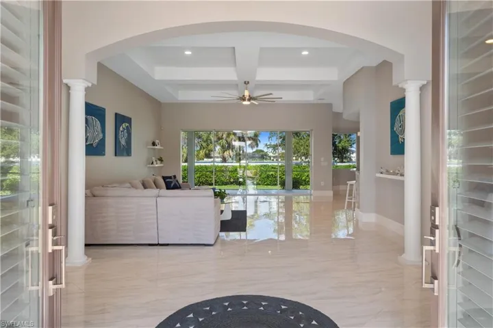Living room featuring coffered ceiling, ceiling fan, decorative columns, and beam ceiling