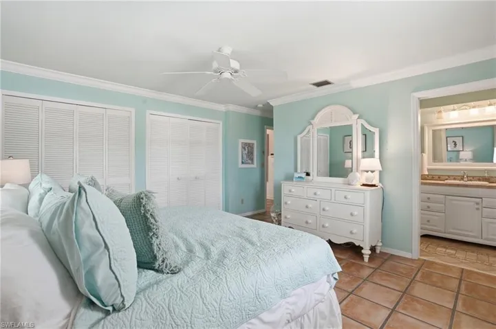 Spacious room featuring a white ceiling fan, crown molding, and two sets of louvered bi-fold closet doors - Virtually Edited Image