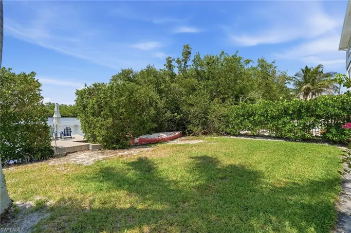 Green lawn area with a concrete patio overlooking the water, featuring lush surrounding foliage and a clear sky - Virtually Edited Image