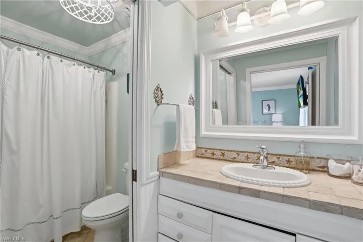 Bathroom featuring a white vanity with an integrated sink, tiled countertop, and a framed mirror - Virtually Edited Image