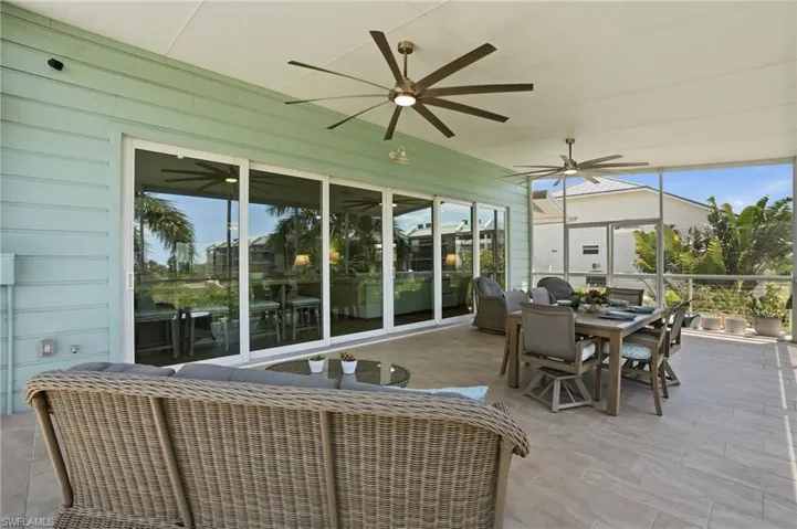 Screened lanai featuring large format tile flooring, multiple ceiling fans, horizontal siding, and multi-panel sliding glass doors - Virtually Edited Image