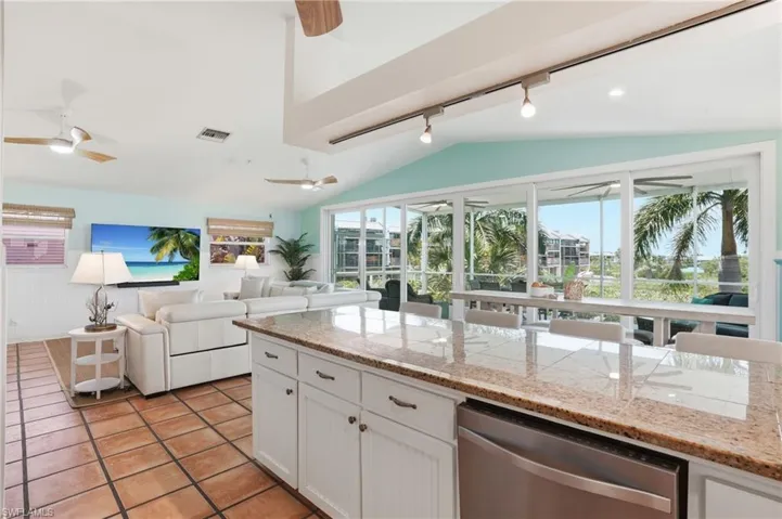 Open-concept living space featuring a vaulted ceiling, track lighting, and a kitchen island with stone-finish countertops - Virtually Edited Image