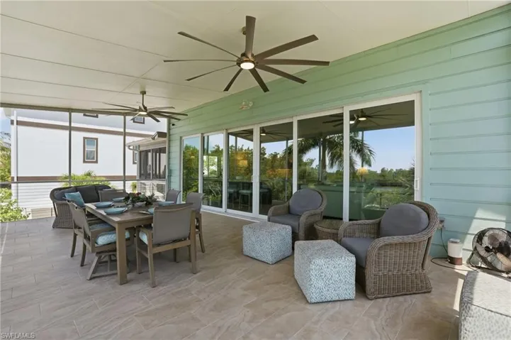 Expansive screened patio featuring large format tile flooring, a pale green siding exterior, multiple ceiling fans with integrated lighting, and a full wall of sliding glass doors - Virtually Edited Image