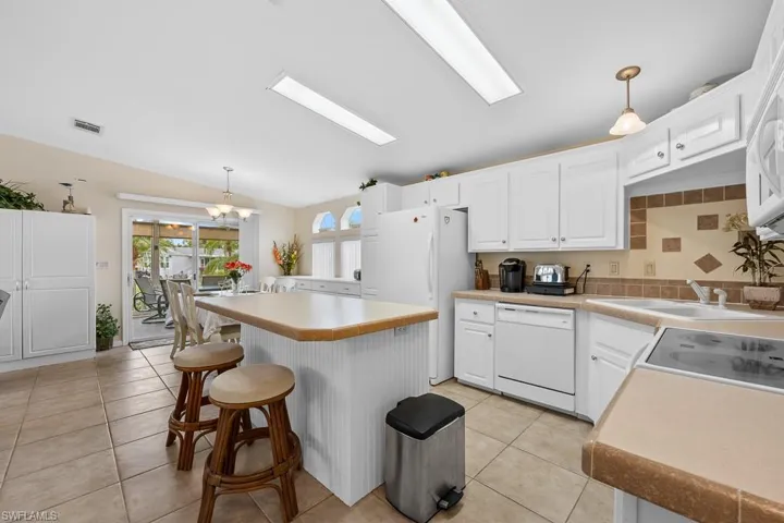 Kitchen featuring decorative light fixtures, white cabinets, a breakfast bar area, light countertops, and light tile patterned floors
