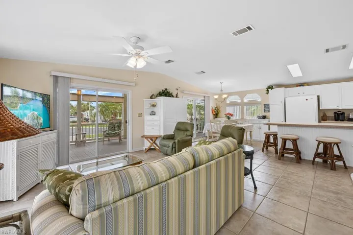 Living area with light tile patterned floors, vaulted ceiling, a ceiling fan, and a chandelier