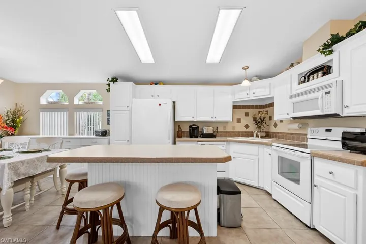 Kitchen featuring white appliances, a breakfast bar area, white cabinets, a kitchen island, and light tile patterned floors