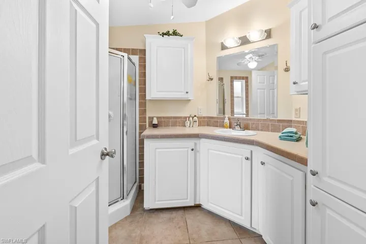 Full bathroom featuring a stall shower, vanity, light tile patterned flooring, and ceiling fan