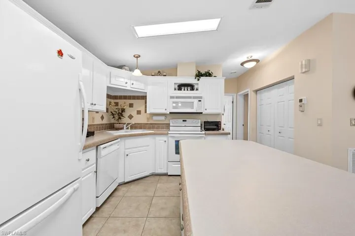 Kitchen with white appliances, white cabinetry, light tile patterned flooring, light countertops, and decorative light fixtures
