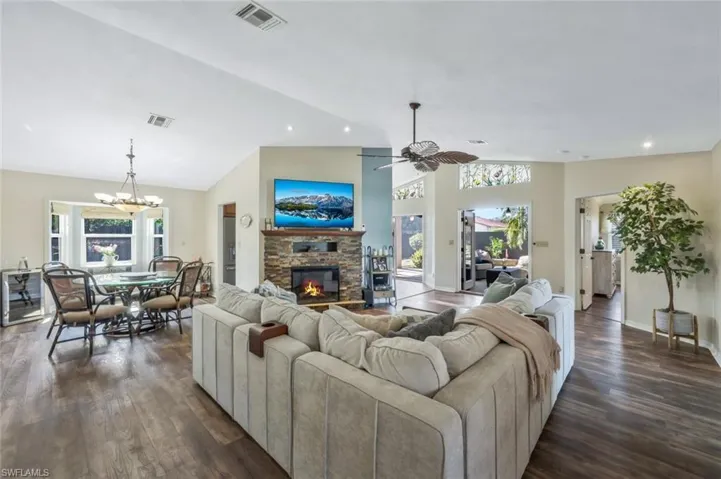 Living room with ceiling fan with chandelier, a fireplace, dark hardwood / wood-style floors, and vaulted ceiling