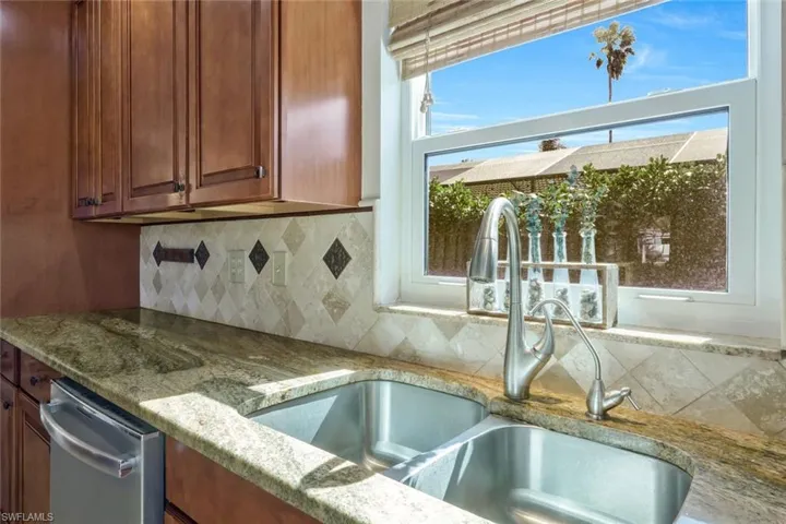 Kitchen featuring sink, stainless steel dishwasher, light stone counters, and decorative backsplash